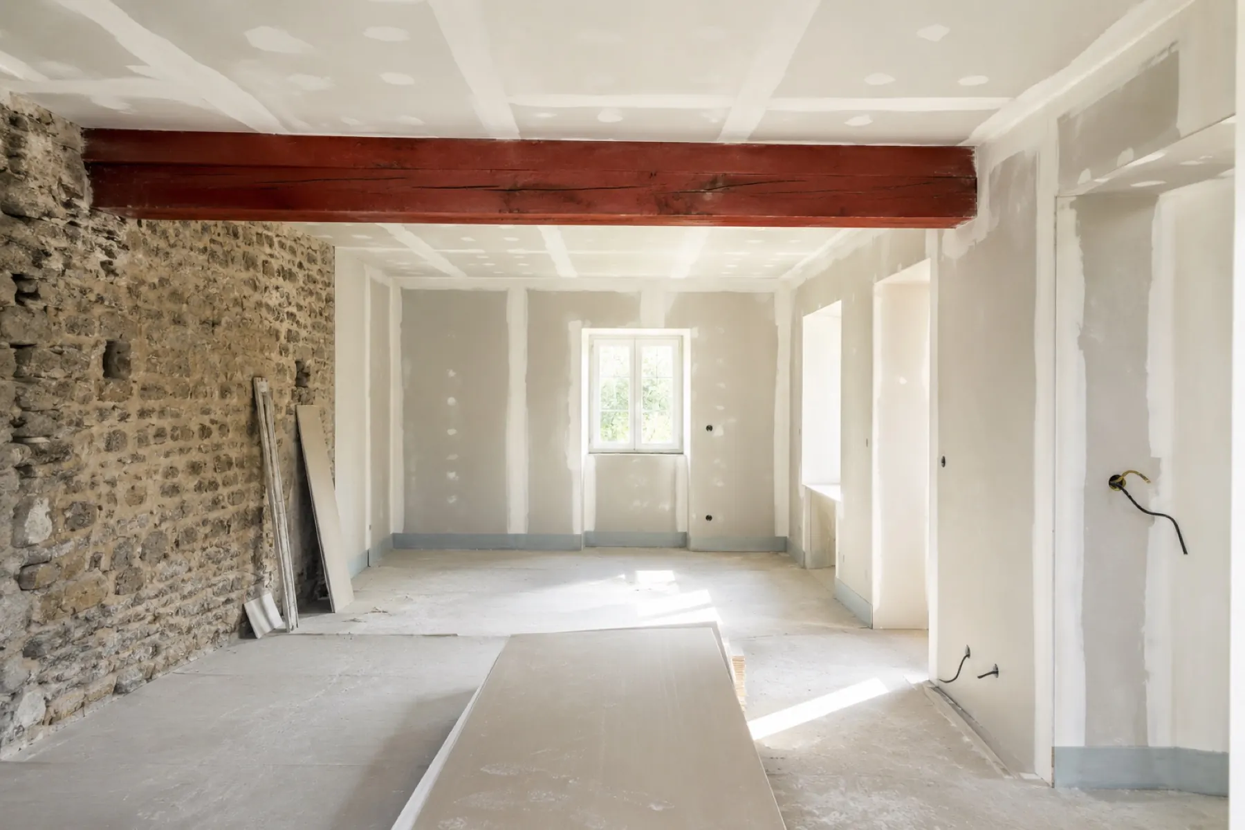 Un chantier avant travaux : plaques de plâtre brutes, bandes apparentes, mur de pierre nu